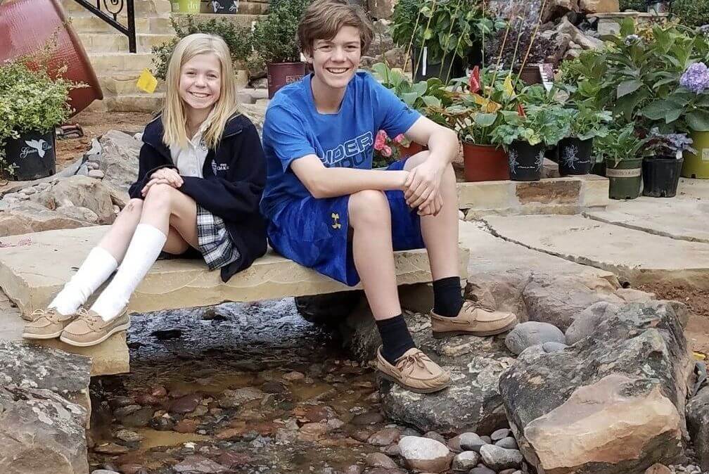 two kids sitting on a bridge over a water feature